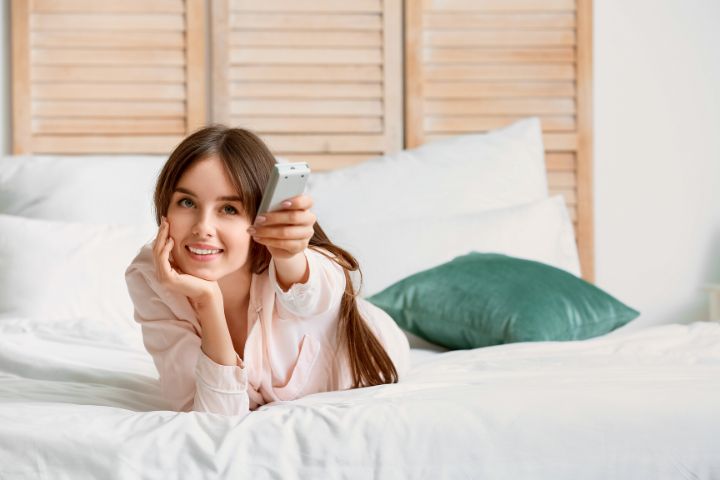 Young Woman with Air Conditioner Remote Control in Bedroom