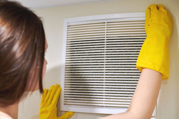 A woman in yellow gloves removing the air con filter