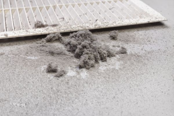 A pile of dust lying on the floor next to a removed aircon duct ventilation grille