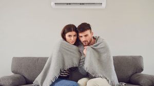 a freezing couple sitting on a sofa below a reverse cycle air conditioner